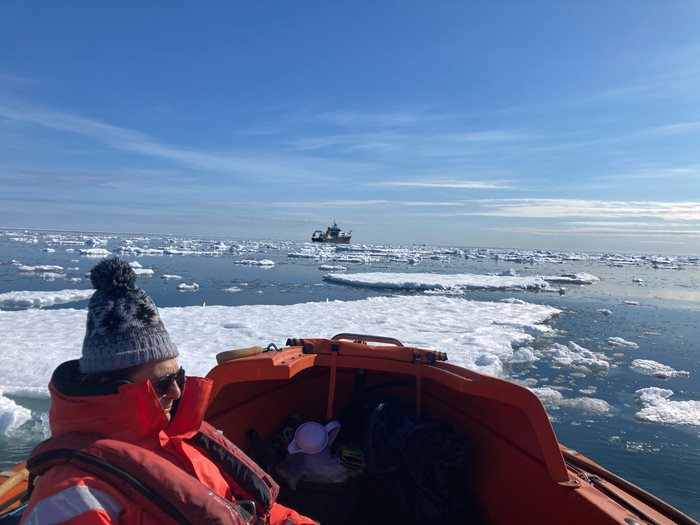 Gavin tilstone on board a small vessel in the sea ice carrying out a survey with the RRS Discovery in the background